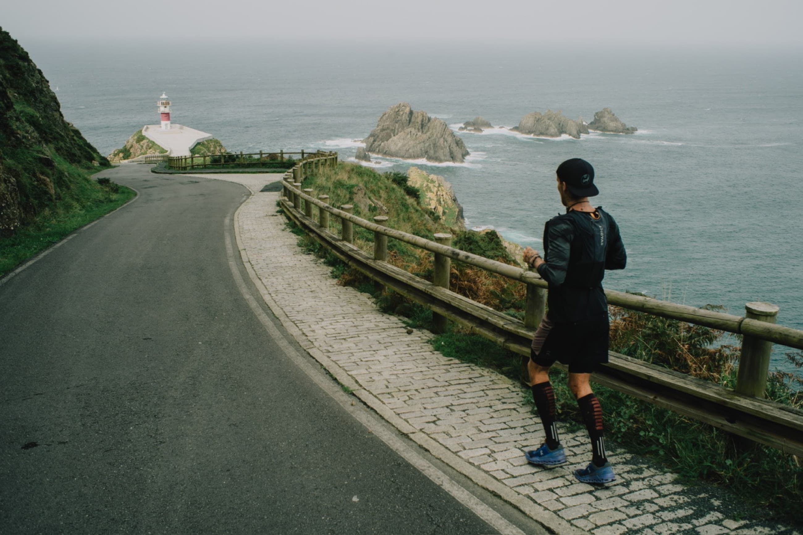 A lone runner on a winding road high above the Atlantic coastline of Portugal, under heavy grey sky.